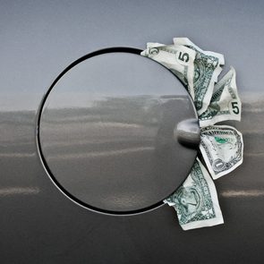 Dollars stuffed into a closed car fuel hatch on a gray vehicle.