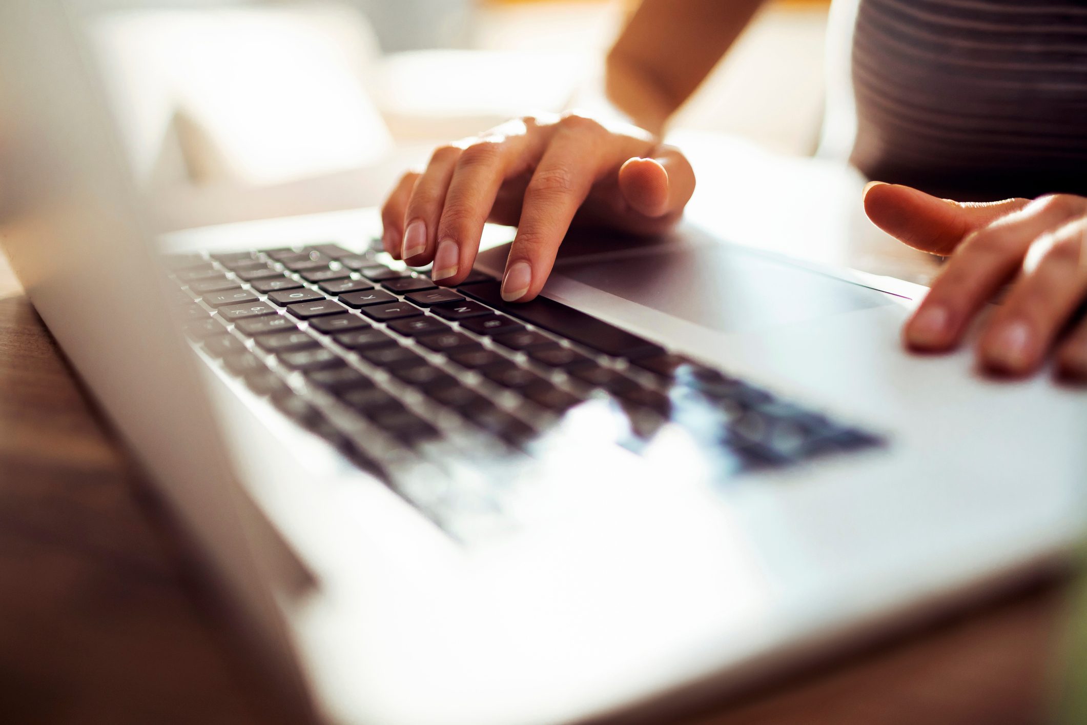 Hands typing on a laptop keyboard, illuminated by natural light in an indoor setting.