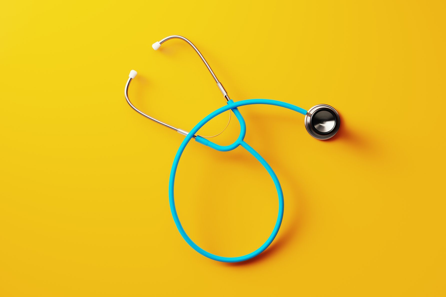 Stethoscope lies coiled on a bright yellow surface, its blue tubing contrasting sharply with the background.